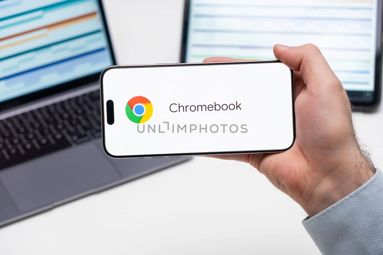 Chromebook application logo on the screen of smart phone in mans hand, laptop and tablet on the table by vladimka