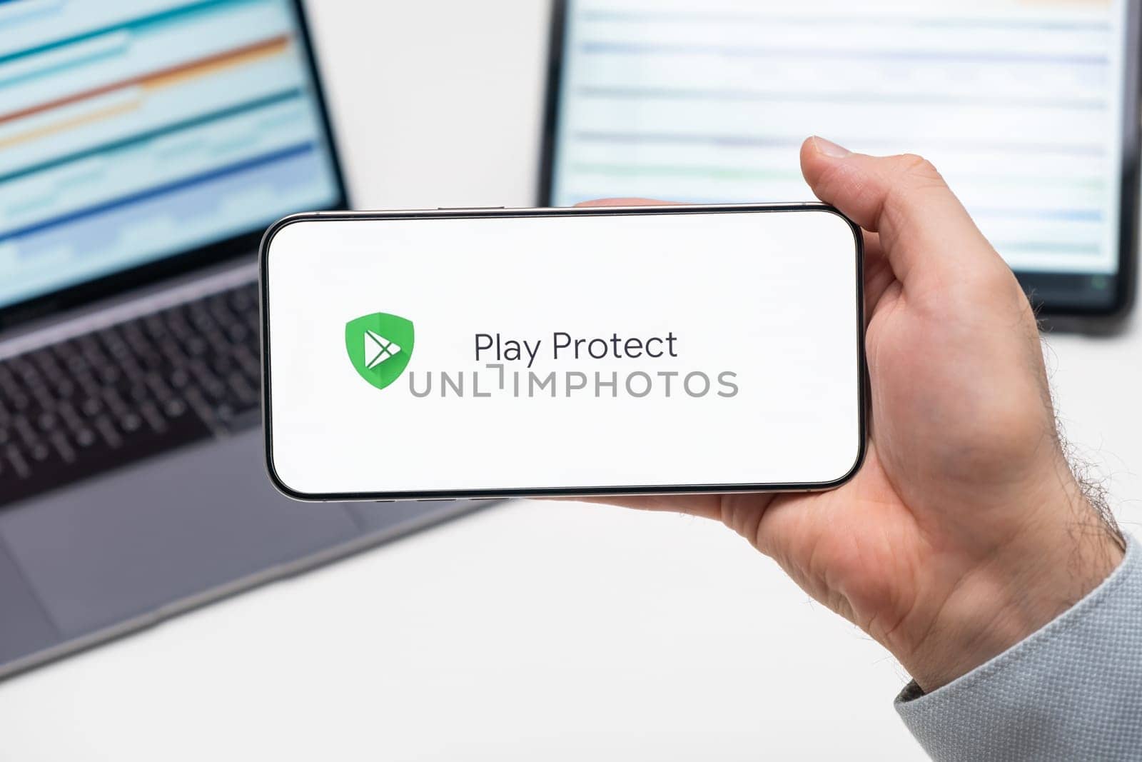 Play Protect logo of app on the screen of mobile phone held by man in front of the laptop and tablet, December 2023, Prague, Czech Republic
