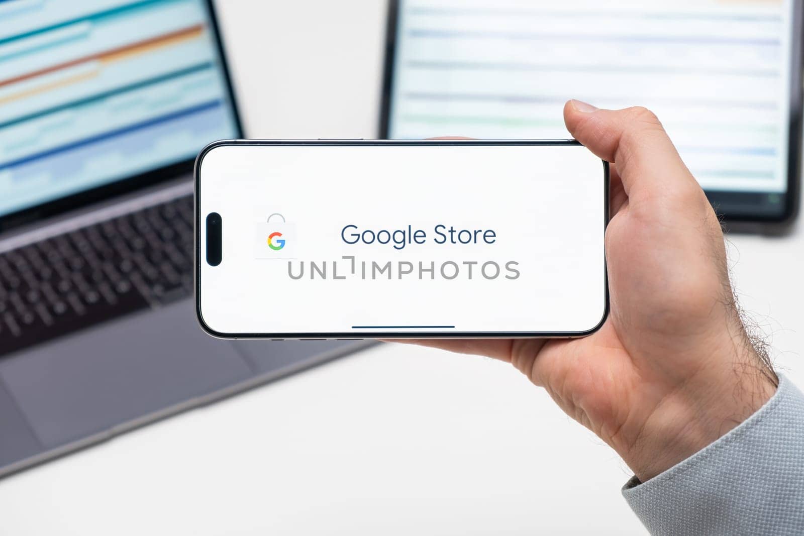 Google store logo of app on the screen of mobile phone held by man in front of the laptop and tablet, December 2023, Prague, Czech Republic