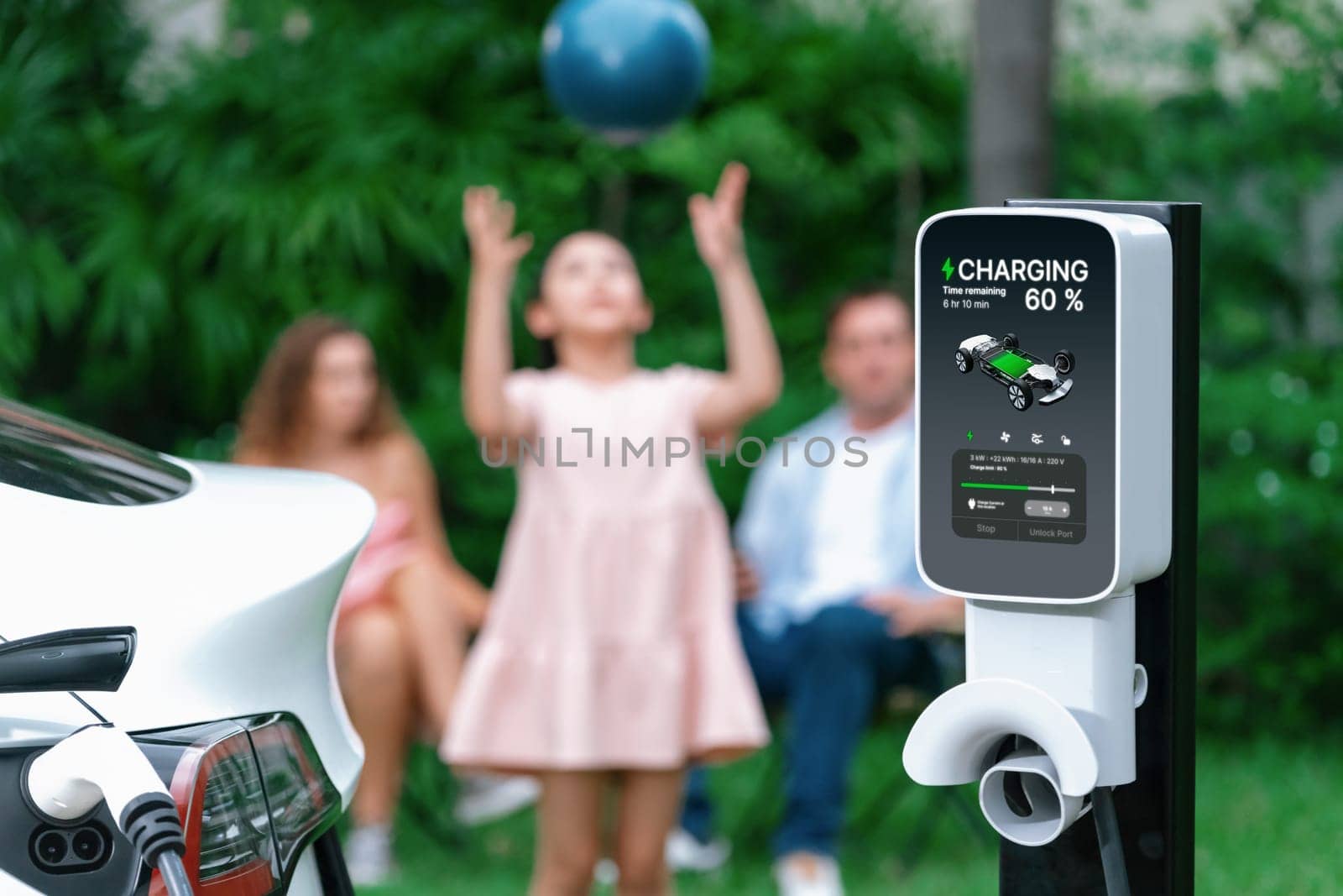 Focus electric vehicle recharge from home charging station on blur background of happy and playful family playing together. EV car using alternative and sustainable energy for better future.Synchronos