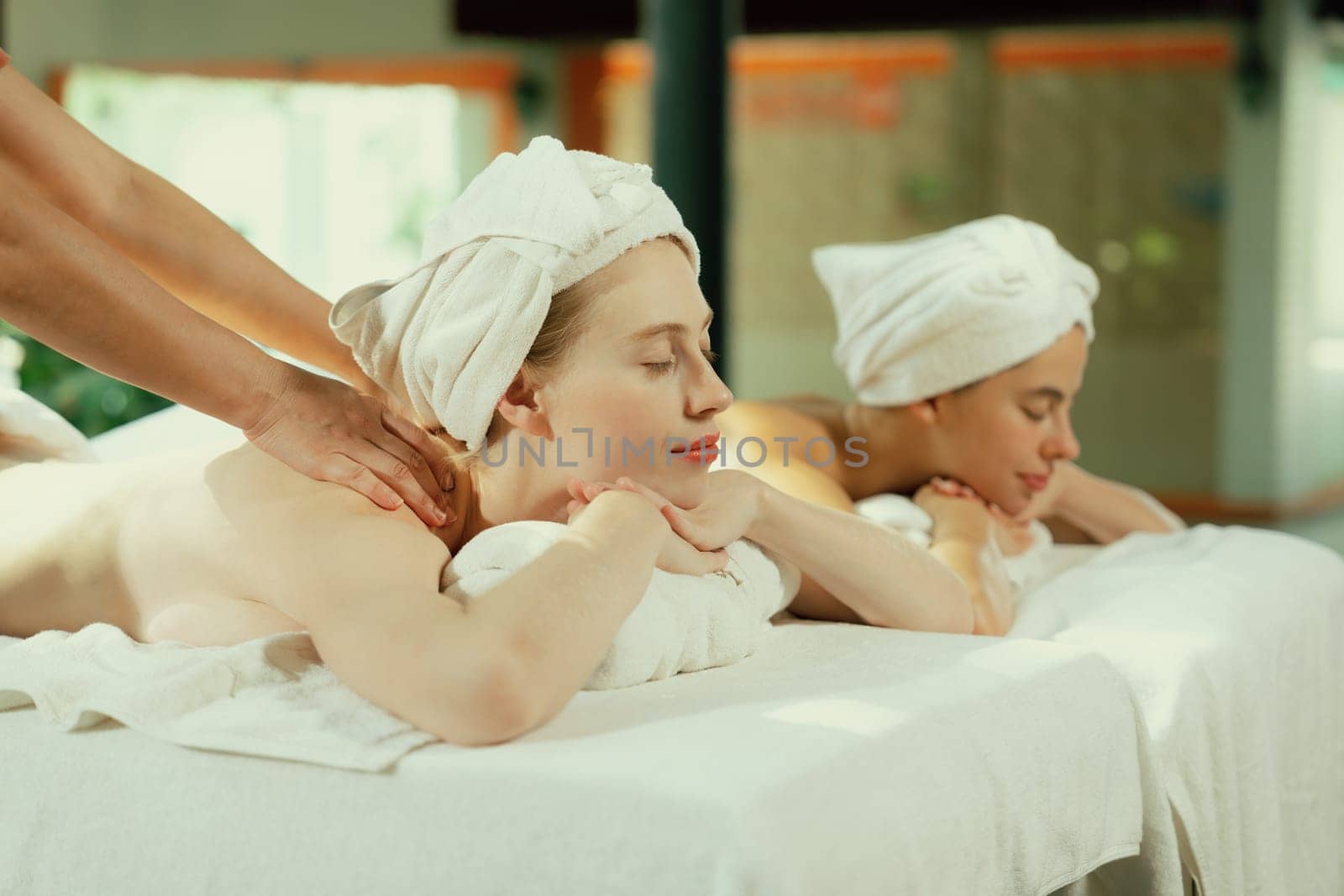 Couple of beautiful young woman lie on white spa bed during having back massage. Attractive caucasian woman having back massage at traditional spa room. Relaxing and healthy concept Tranquility.