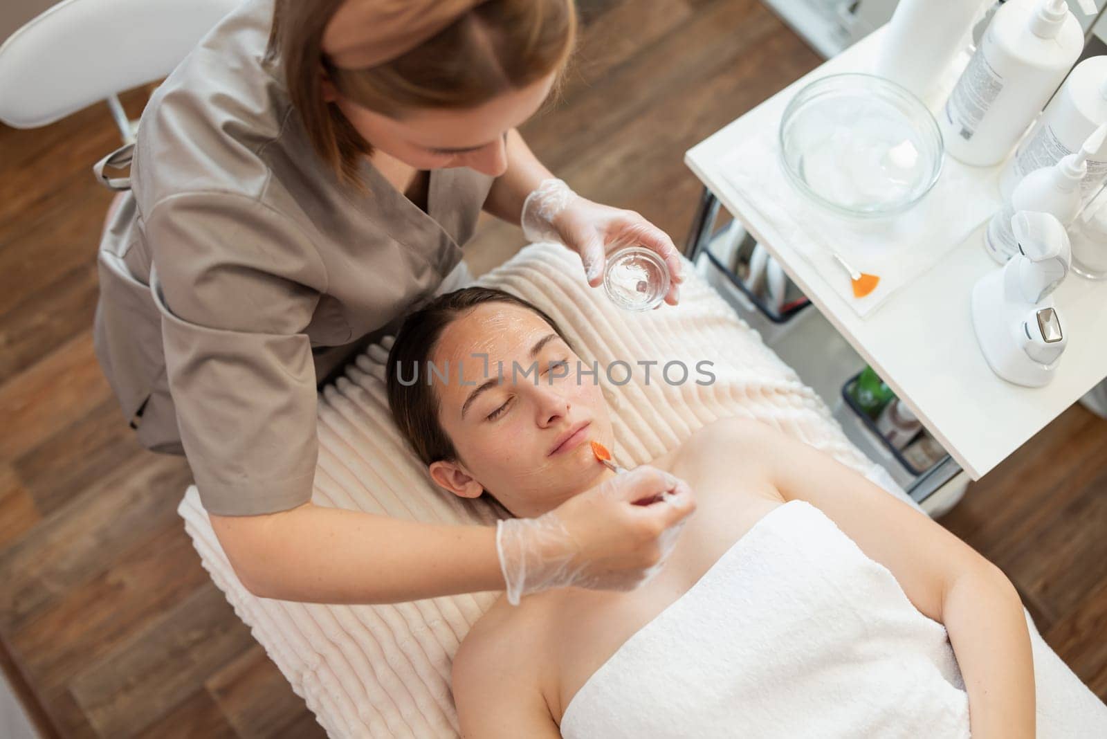Top-down shot of a doctor applying gel for opening pores on face of a client of a cosmetology clinic before ultrasound or mechanical cleaning by VitaliiPetrushenko