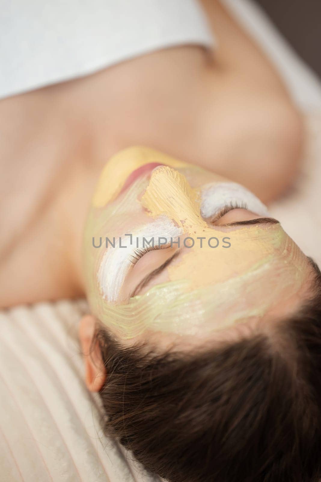 Young girl with closed eyes relaxing with facial cosmetological masks while they moisturizing, cleansing, exfoliating her skin by VitaliiPetrushenko