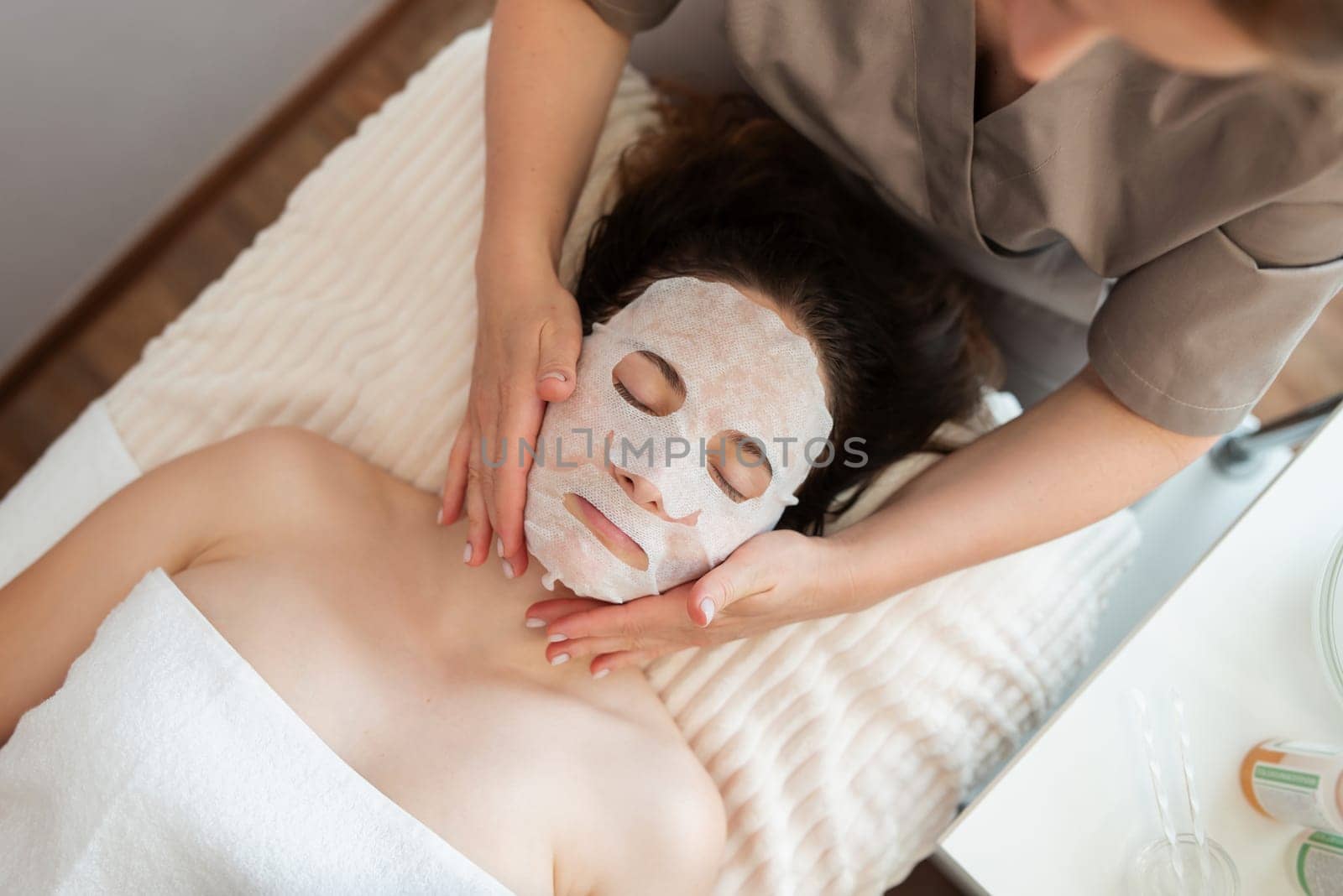 Cosmetologist beautician putting on a mask to a girl client by VitaliiPetrushenko