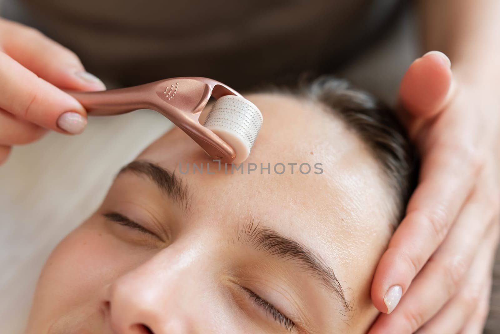 Doctor cosmetologist using roller with micro needles for stimulation of skin regeneration and introduction of various rejuvenating drugs