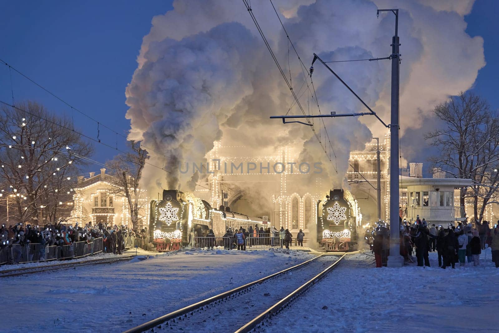 Russia, Peterhof, 07 January 2024: Two Santa Claus Trains leave the magically decorated building of the New Peterhof station, huge steam clubs, many people, incredible lighting. High quality photo