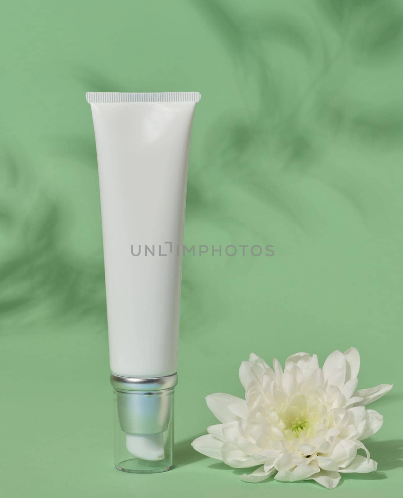 White plastic tube with a transparent cap and dispenser on an green background, container for cosmetics by ndanko