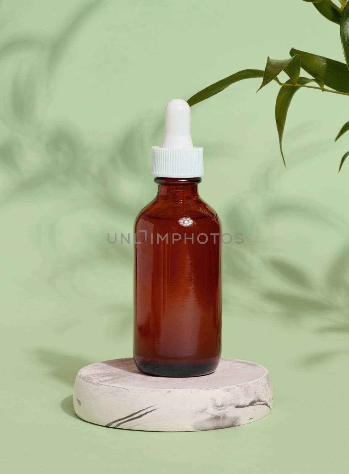 A glass brown bottle with a dropper on a green background, a container for cosmetic products. 