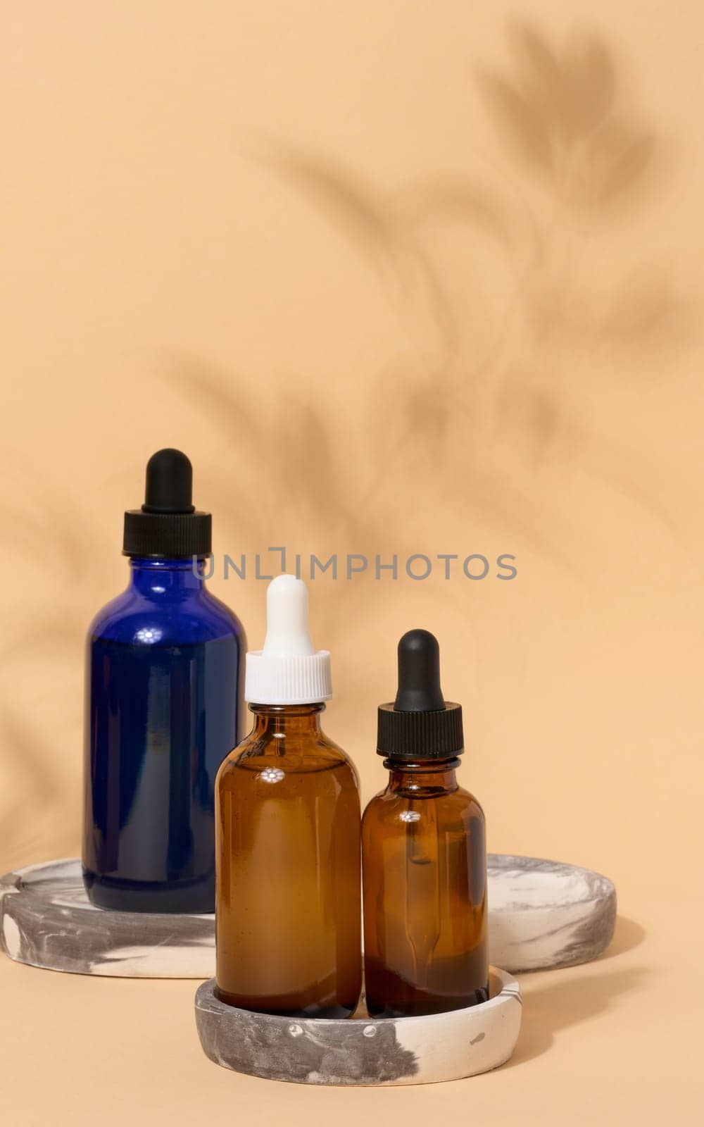 Glass bottles with pipettes on a beige background with a shadow from a branch. Containers for cosmetics by ndanko