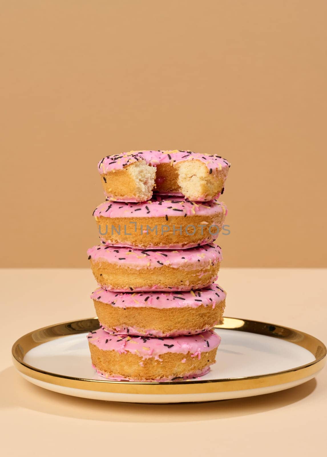 Donut covered with pink glaze and sprinkled with colorful sprinkles on a round plate, brown background