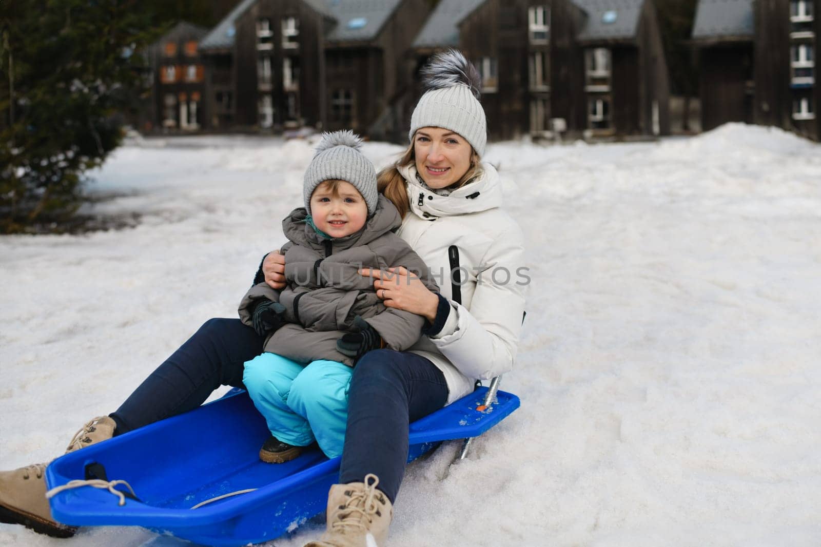 A mother with son sledding in the snow by Godi