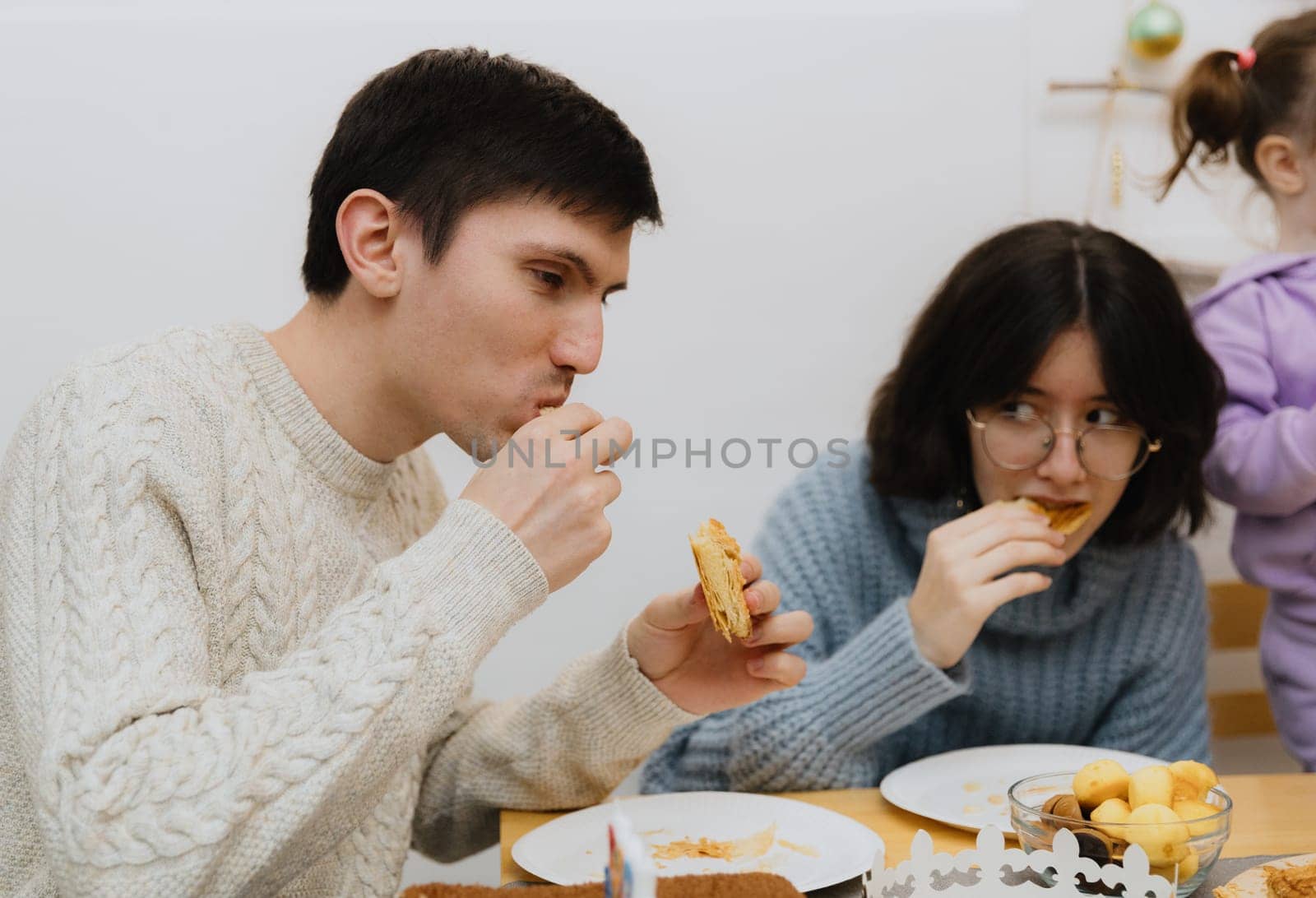 One young handsome Caucasian guy takes a surprise out of his mouth from an eaten piece of royal galette, sitting at the table with his family, close-up side view.