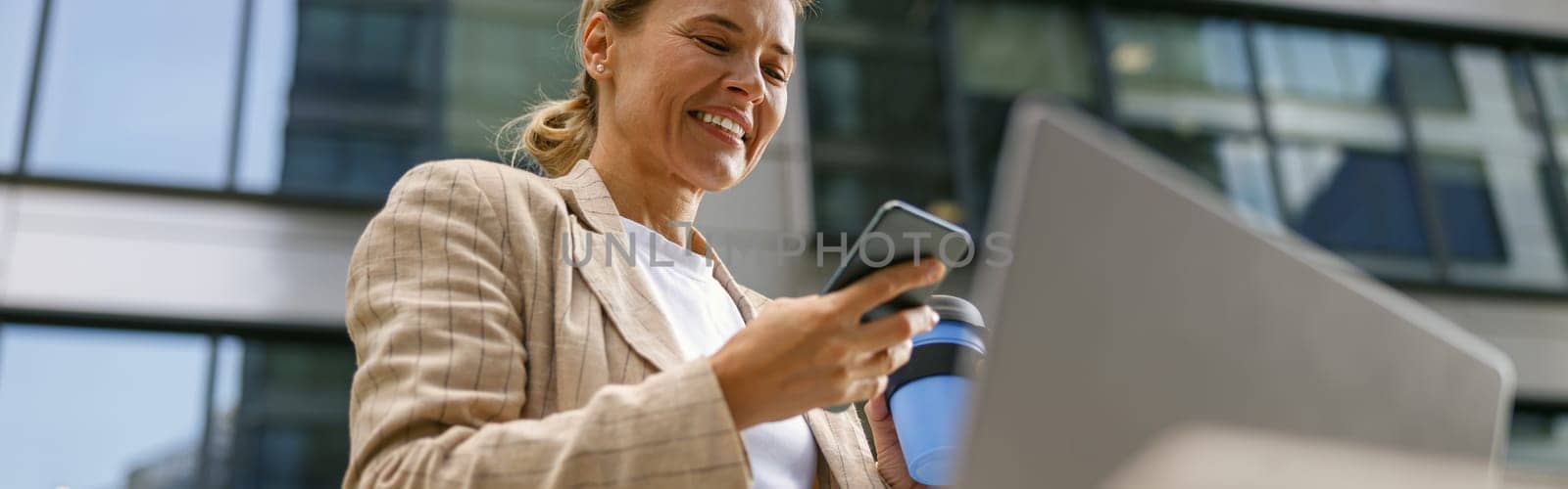 Businesswoman is using phone and work on laptop outside of office. Distance work concept by Yaroslav_astakhov