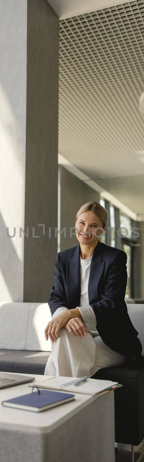 Pretty female entrepreneur working on laptop sitting in modern office hall and looks camera