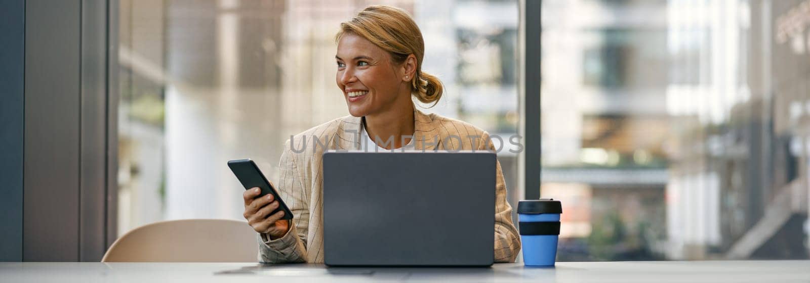 Stylish business woman use phone while sitting in modern coworking and working on laptop