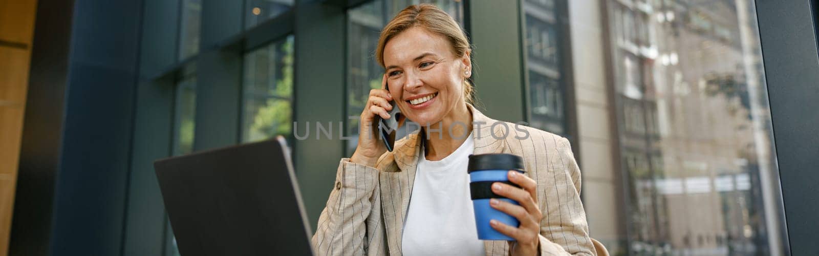 Smiling businesswoman talking on phone with client while working on laptop in office
