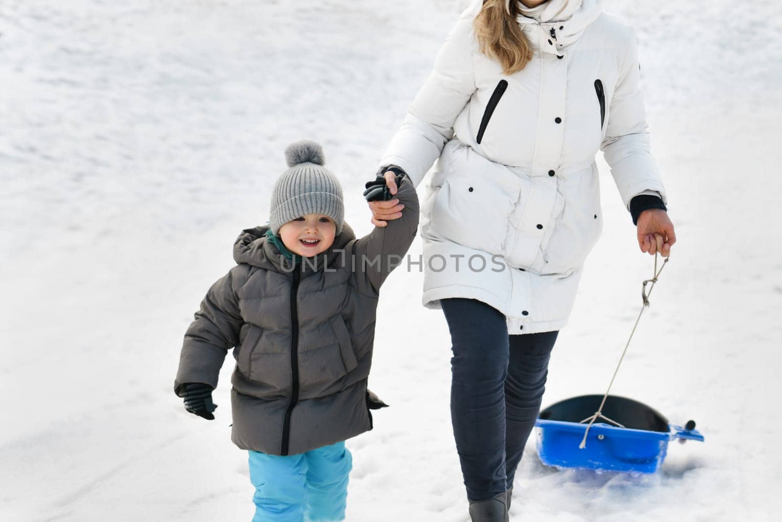 A mother with son sledding in the snow by Godi