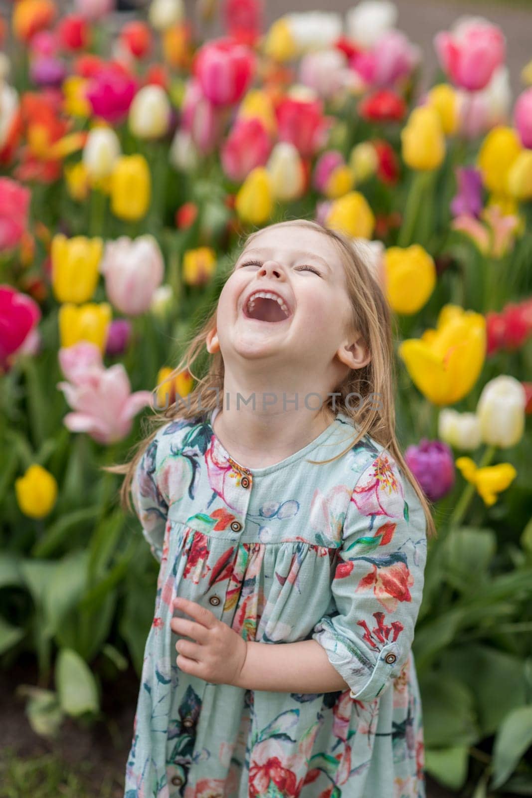 Happy girl laughs in a park with the tulips field by Godi