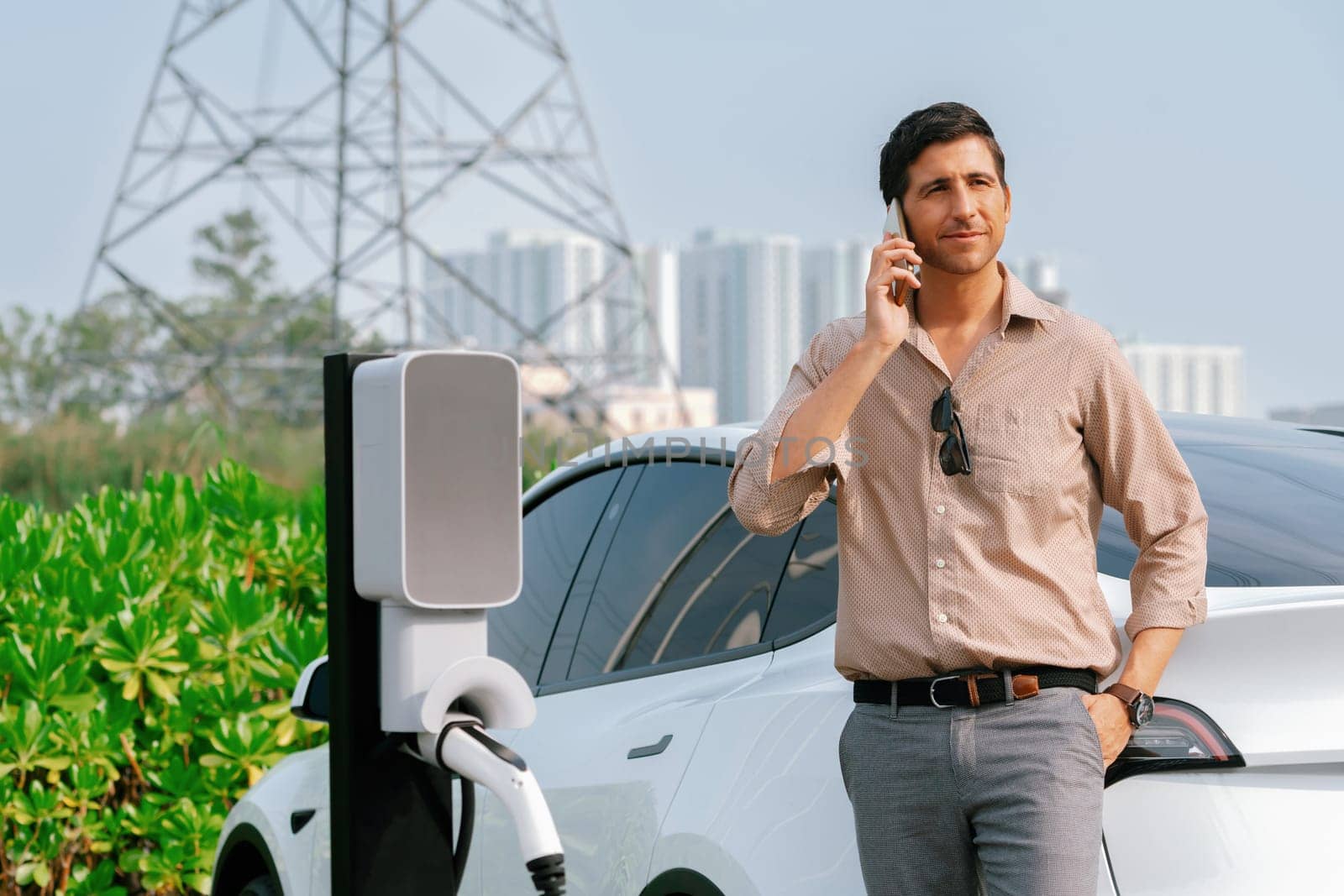 Man talking on the phone while recharge EV car at charging station. Expedient by biancoblue