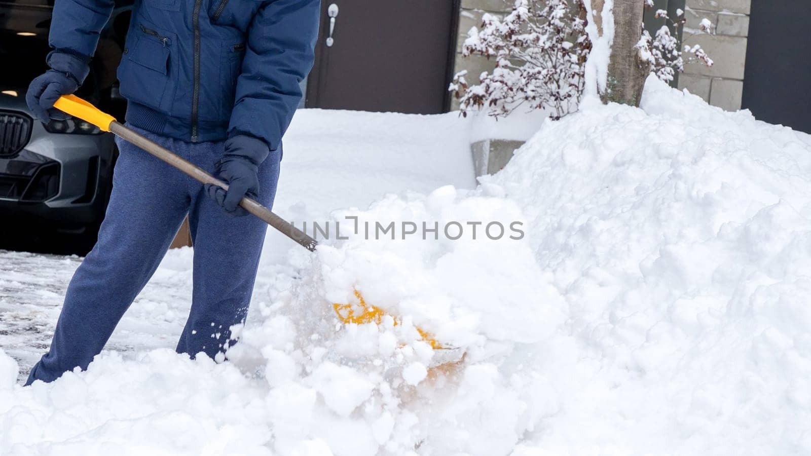 Man shoveling snow off of his driveway after a winter storm in Canada. Man with snow shovel cleans sidewalks in winter. Winter time. by JuliaDorian