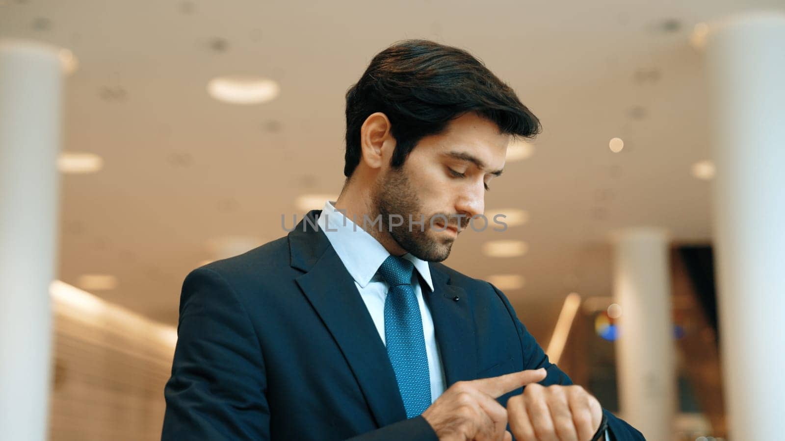 Caucasian smart business man looking at watch while waiting colleague. Executive manager wearing suit while standing at mall with blurred background. Investor wear blue suit check time. Exultant.