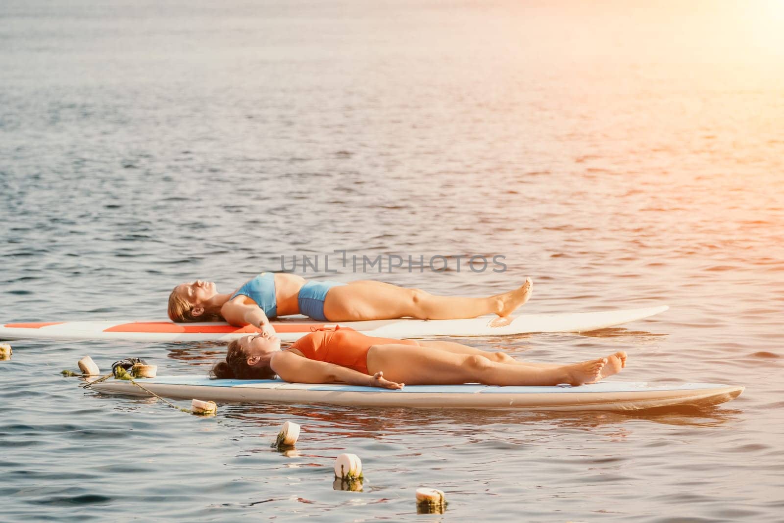 Woman sup yoga. Middle age sporty woman practising yoga pilates on paddle sup surfboard. Female stretching doing workout on sea water. Modern individual hipster outdoor summer sport activity