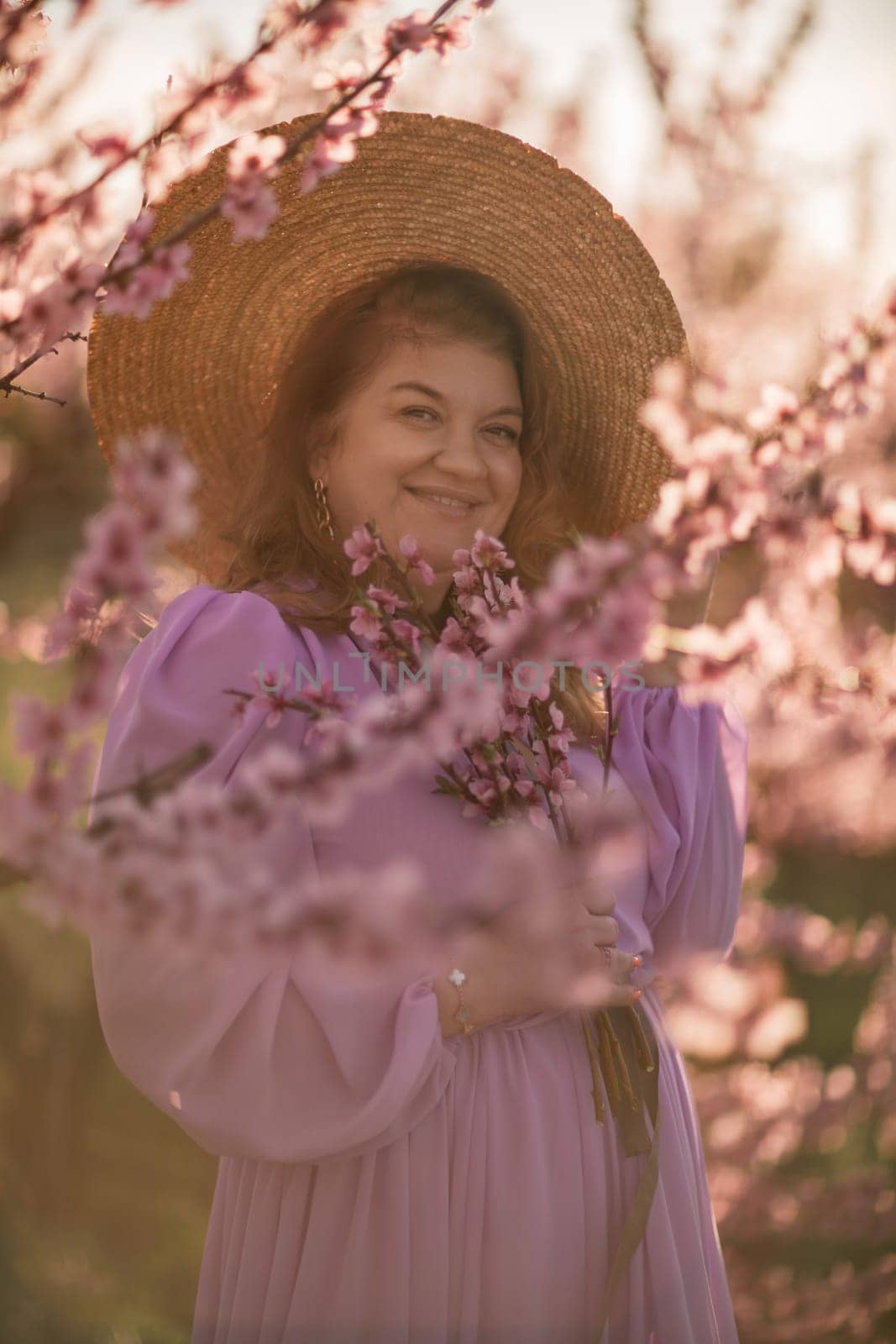 Woman blooming peach orchard. Against the backdrop of a picturesque peach orchard, a woman in a long pink dress and hat enjoys a peaceful walk in the park, surrounded by the beauty of nature. by Matiunina