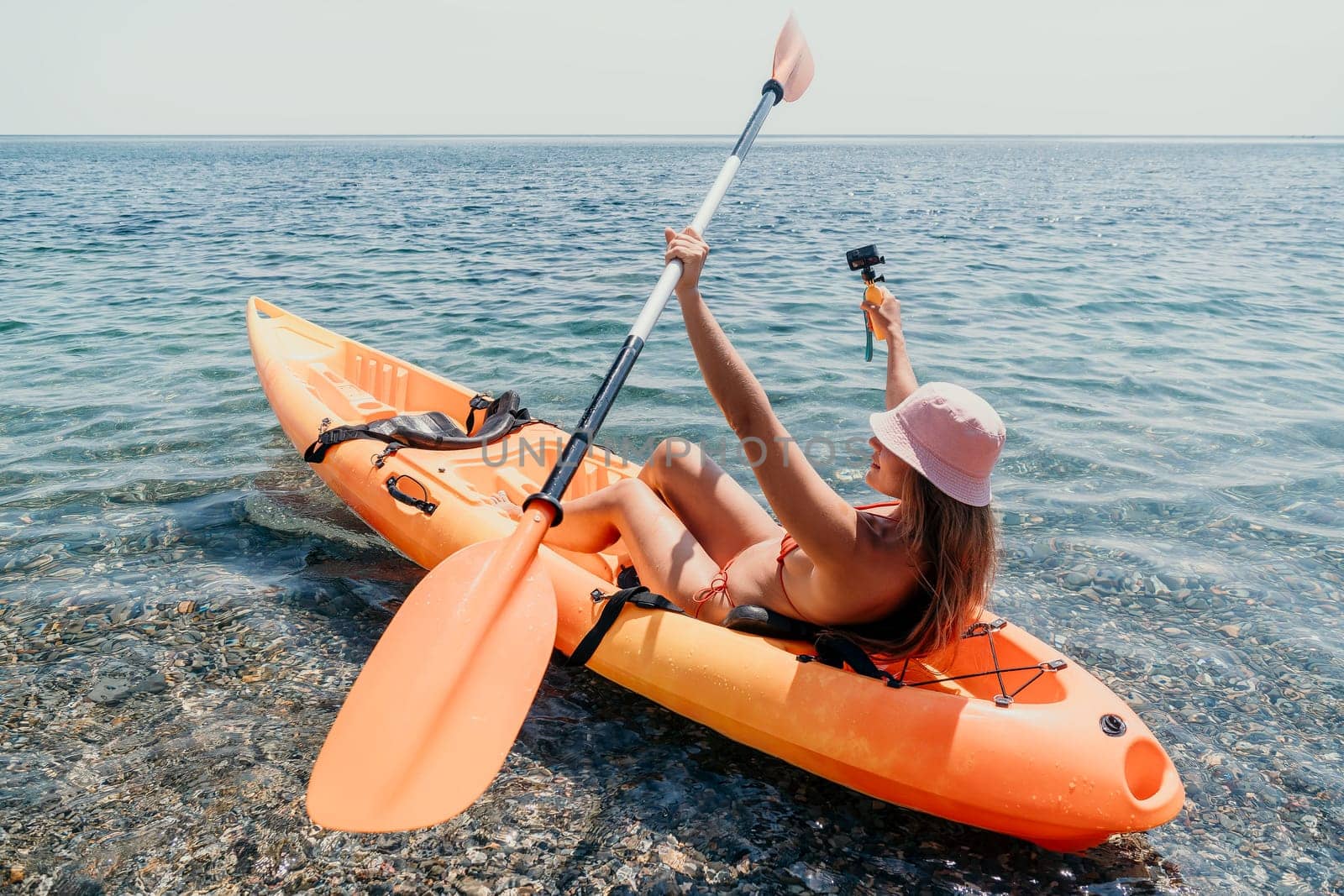 Happy smiling woman in kayak on ocean, paddling with wooden oar. Calm sea water and horizon in background