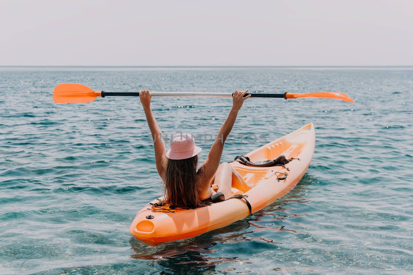 Happy smiling woman in kayak on ocean, paddling with wooden oar. Calm sea water and horizon in background