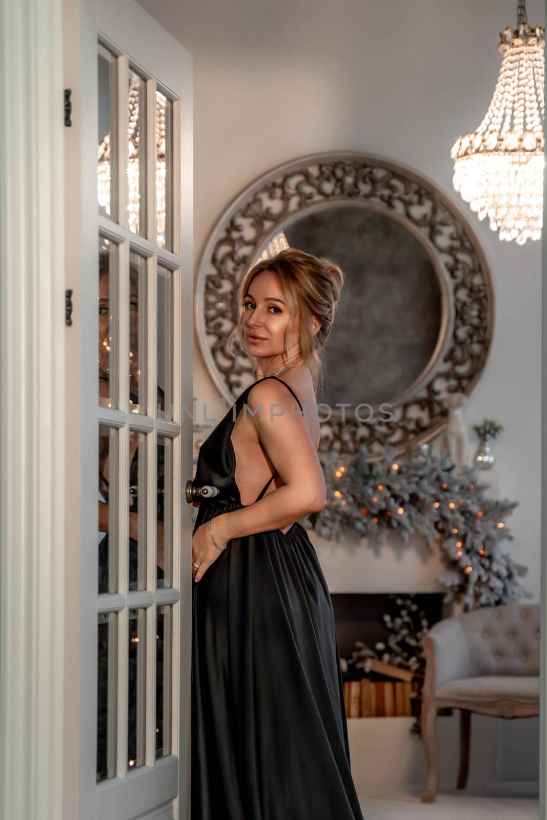 Portrait of a wealthy mature woman with evening make-up and hairstyle posing in a black dress on the background of the Christmas room. Luxurious lifestyle. Christmas holidays concept by Matiunina