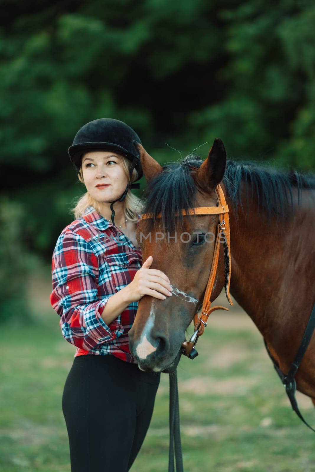 Happy blonde with horse in forest. Woman and a horse walking through the field during the day. Dressed in a plaid shirt and black leggings