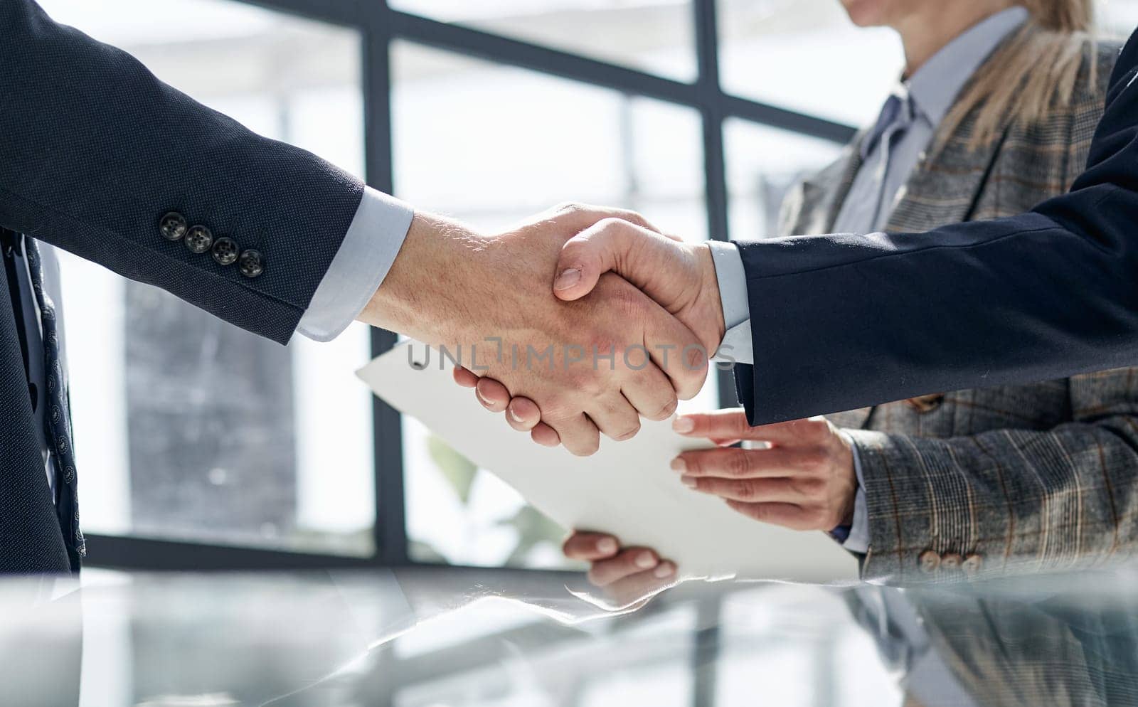 Two business people shaking hands in front of their colleagues by Prosto