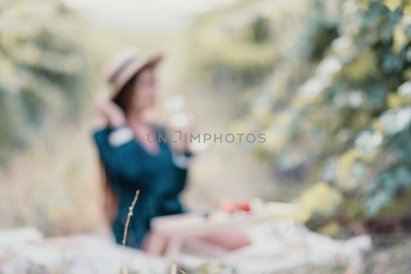 Abstract defocused woman picnic vineyard. Happy woman with a glass of wine at a picnic in the vineyard, wine tasting at sunset and open nature in the summer. Romantic dinner, fruit and wine. by panophotograph