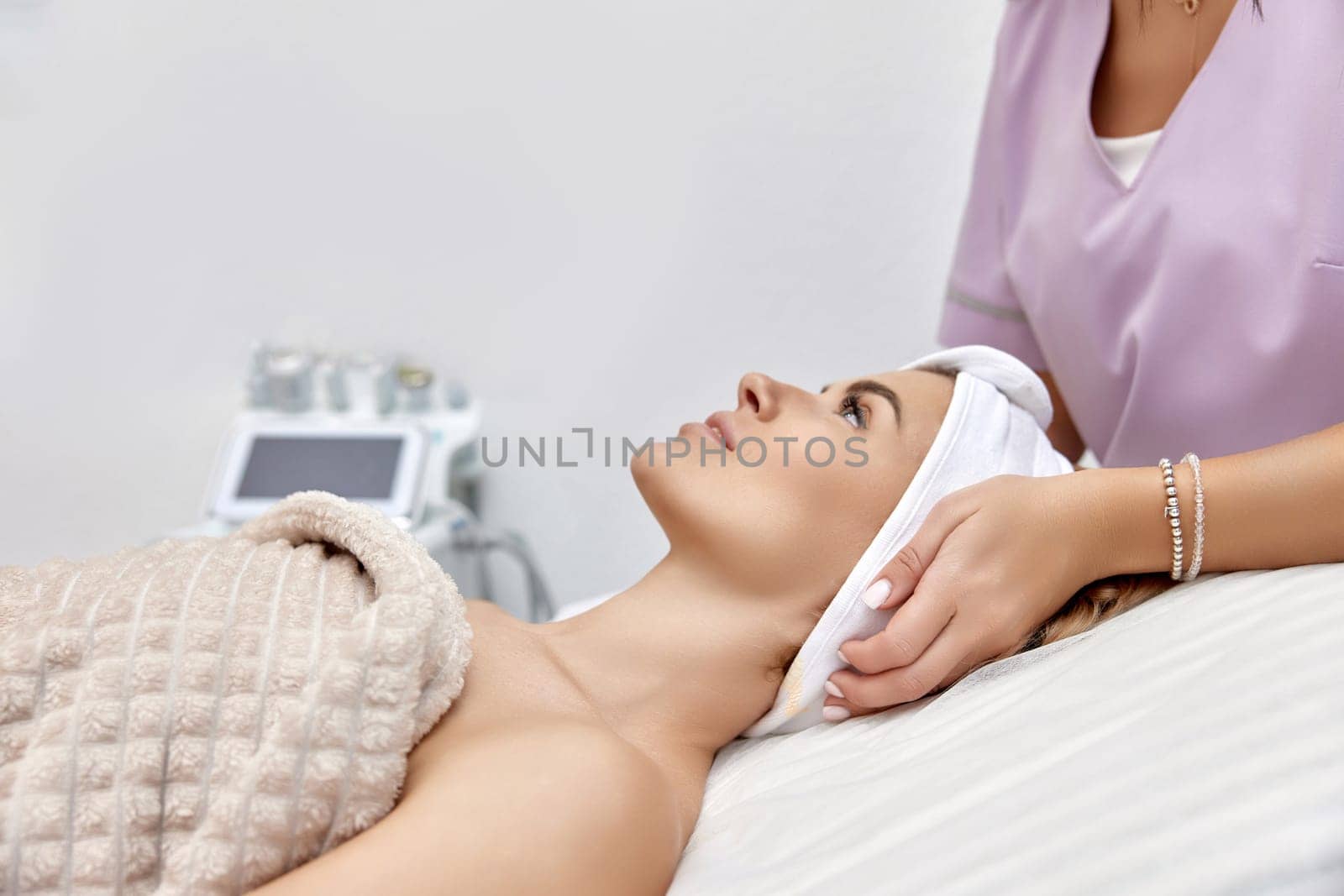 Cosmetologist putting white headband towel on female patient by erstudio