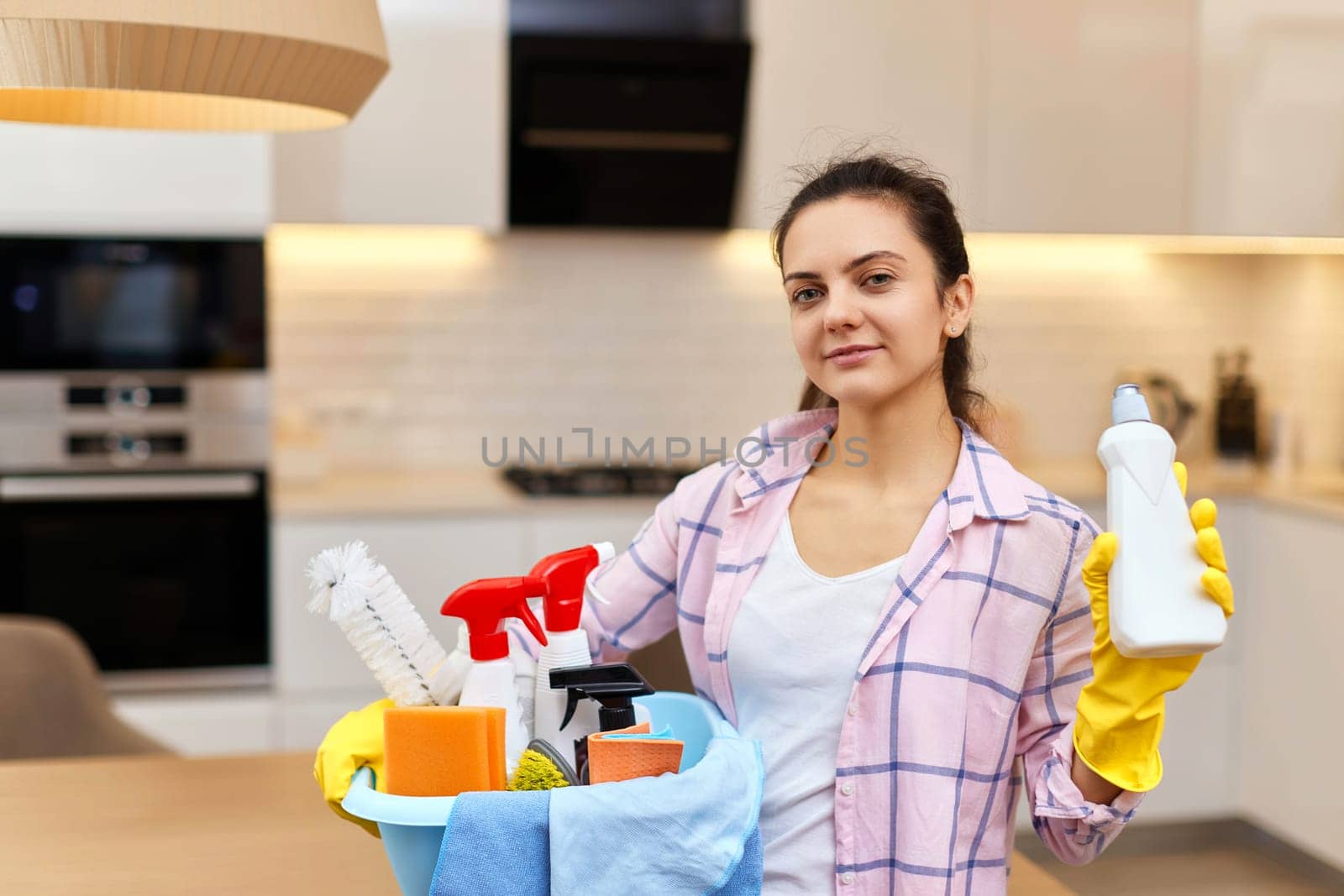Woman in rubber protective yellow gloves holding bucket with cleaning detergents and rags . house chores.