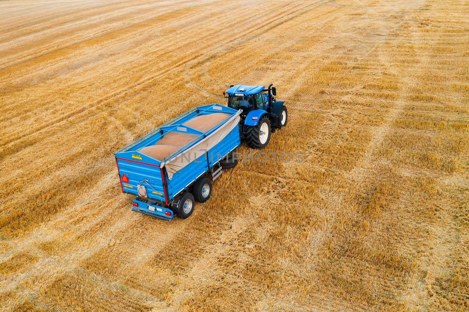 A tractor diligently pulls a trailer behind it as it traverses across a vast field, showcasing ongoing agricultural activities.