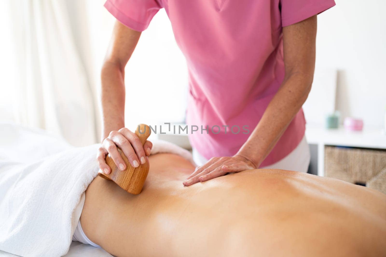 Crop therapist massaging back of customer lying on massage table during wood therapy session in modern physiotherapy clinic