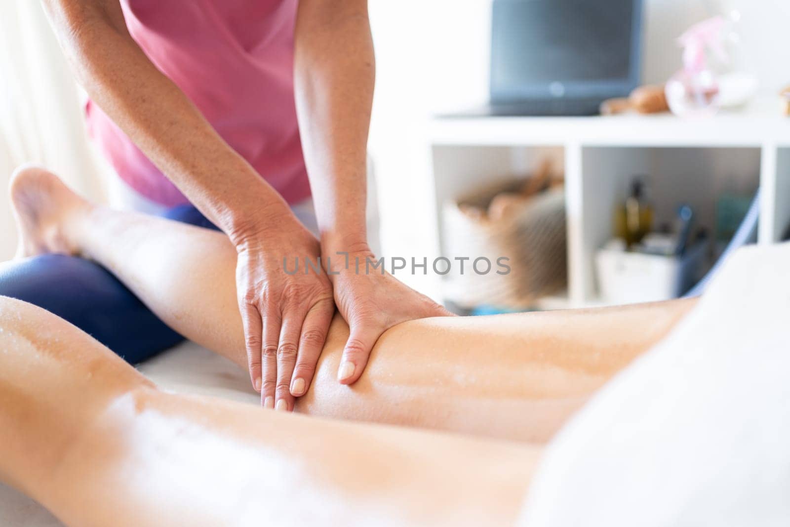 Crop female masseuse doing massage to leg of client in clinic by javiindy