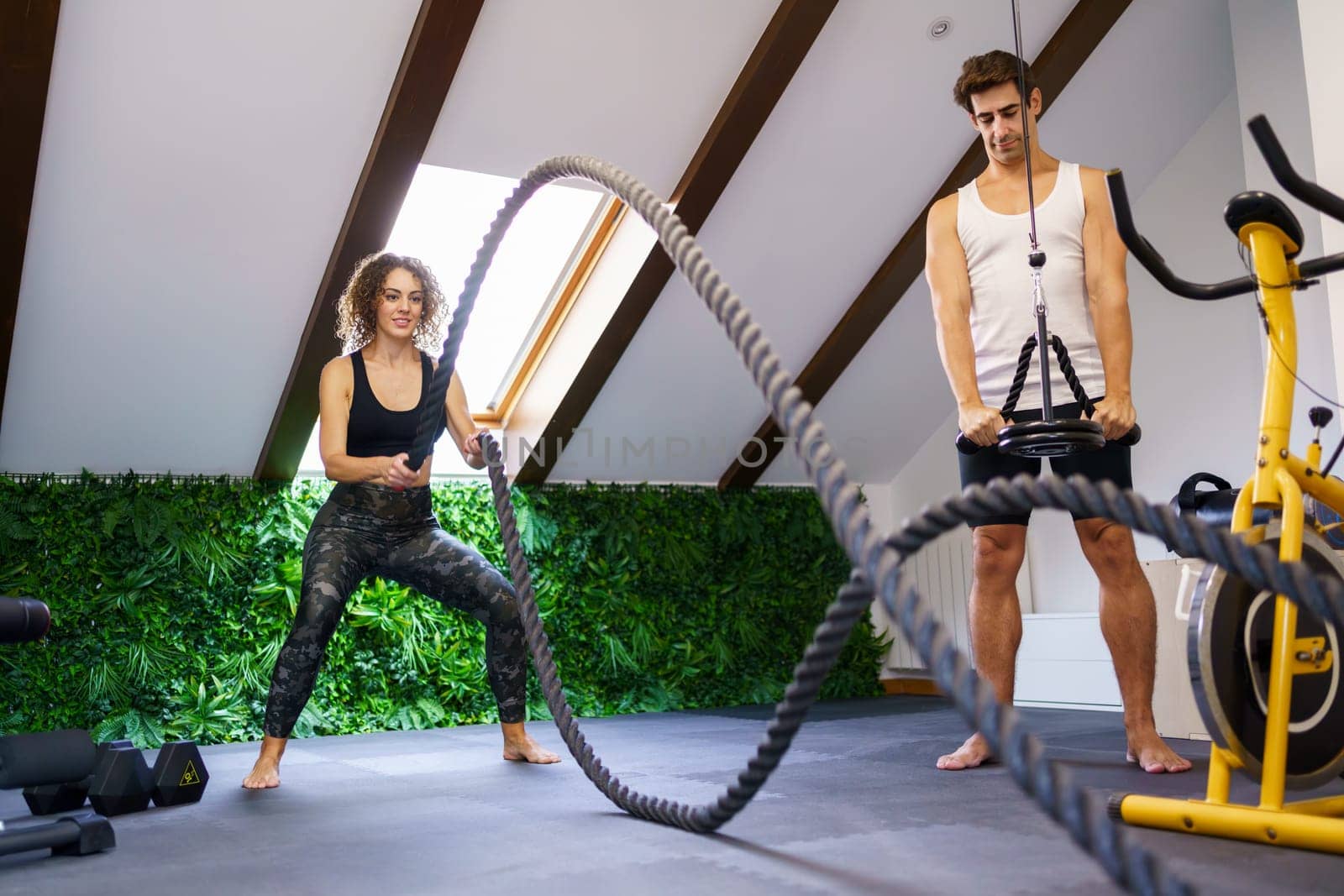 Smiling sportswoman doing exercise with battle ropes in fitness club by javiindy