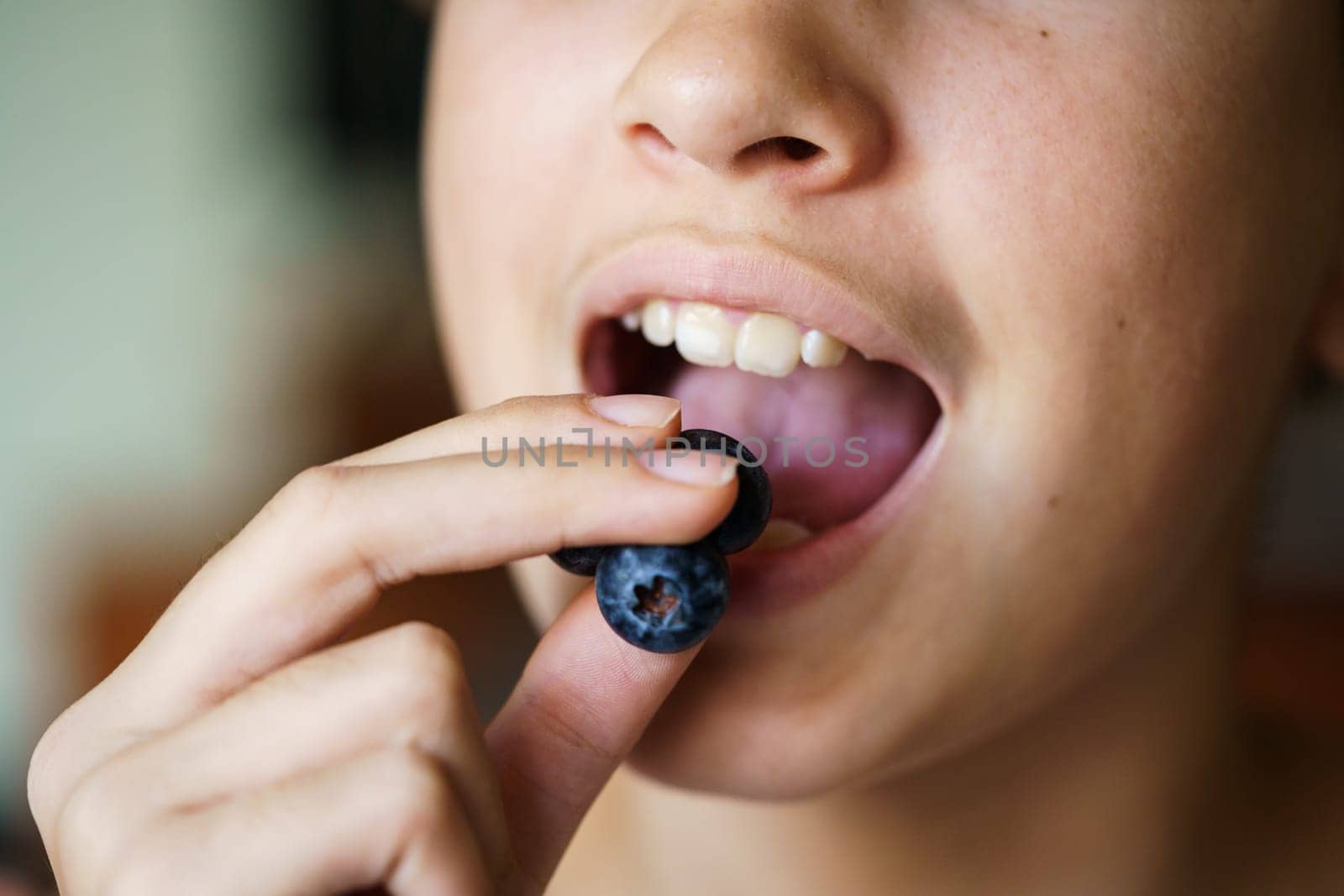 Closeup of unrecognizable teenage girl with mouth open eating yummy blueberries at home
