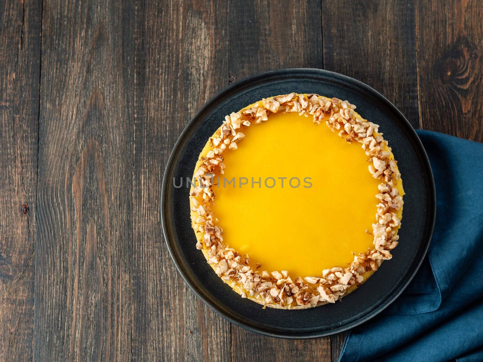 Lemon tart or lemon cake decorated chopped walnuts. Delicious whole lemon pie on wooden background. Aesthetic of traditional classic french lemon tart, recipe idea. Top view, copy space, rustic background