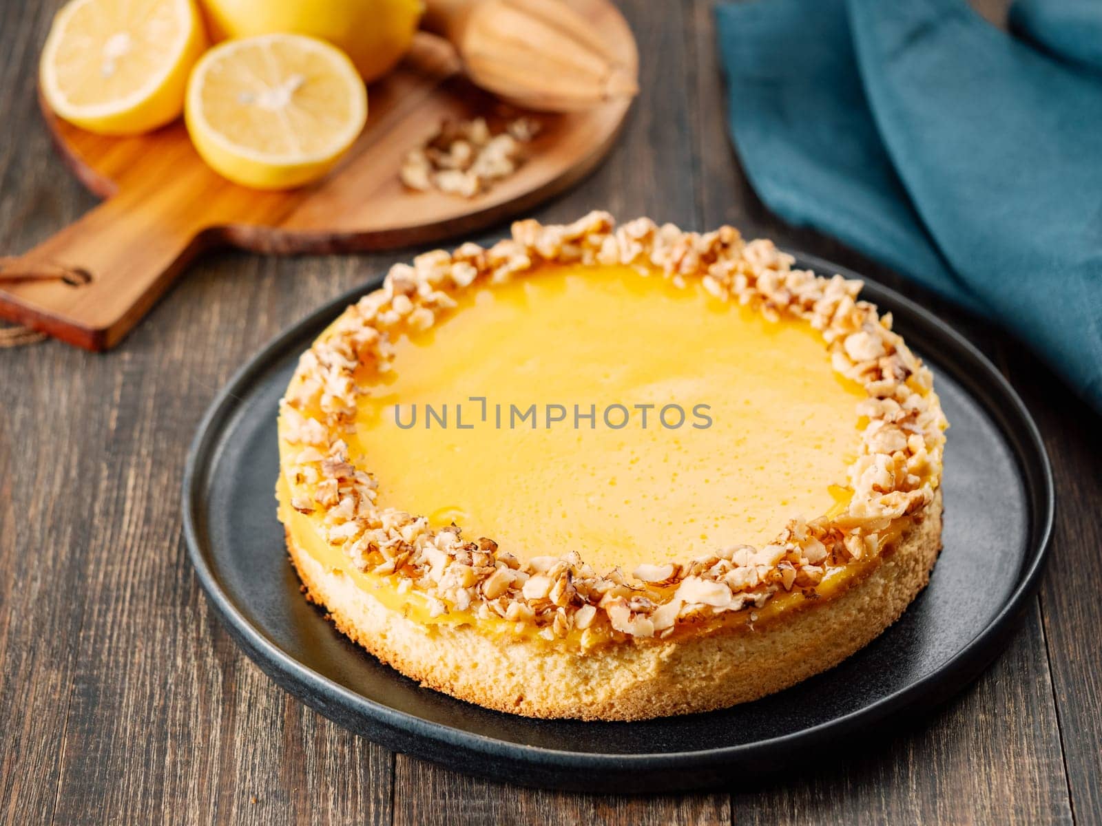 Vegan lemon tart or lemon cake, modernly decorated chopped walnuts. Delicious whole lemon pie on plate on wooden background. Aesthetic of traditional classic french yellow tart with lemon curd recipe