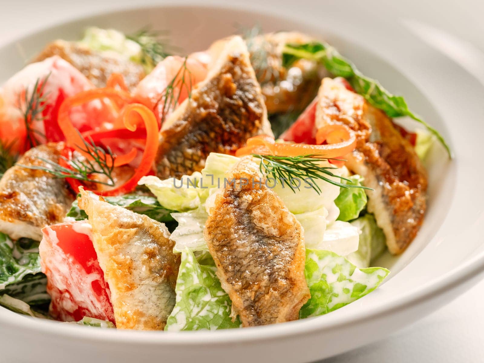 Delicious salad with fried baked smelt fish. Fried fish salad with fresh green lettuce, tomatoes, bell pepper. Ketogenic, keto or paleo diet lunch bowl. Ideas and recipe for fish lunch dishes menu