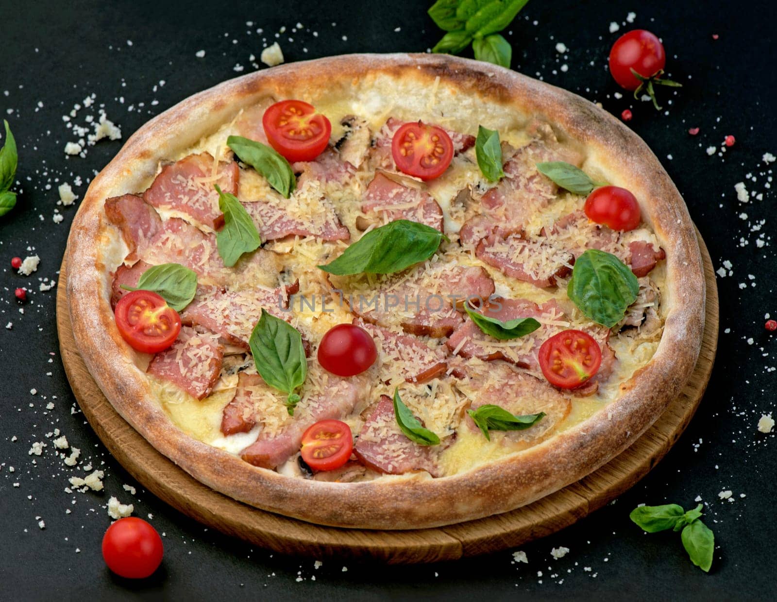 Pizza with cheese, ham, cherry tomatoes and basil on a black background. Delicious pizza with meat and cheese by aprilphoto