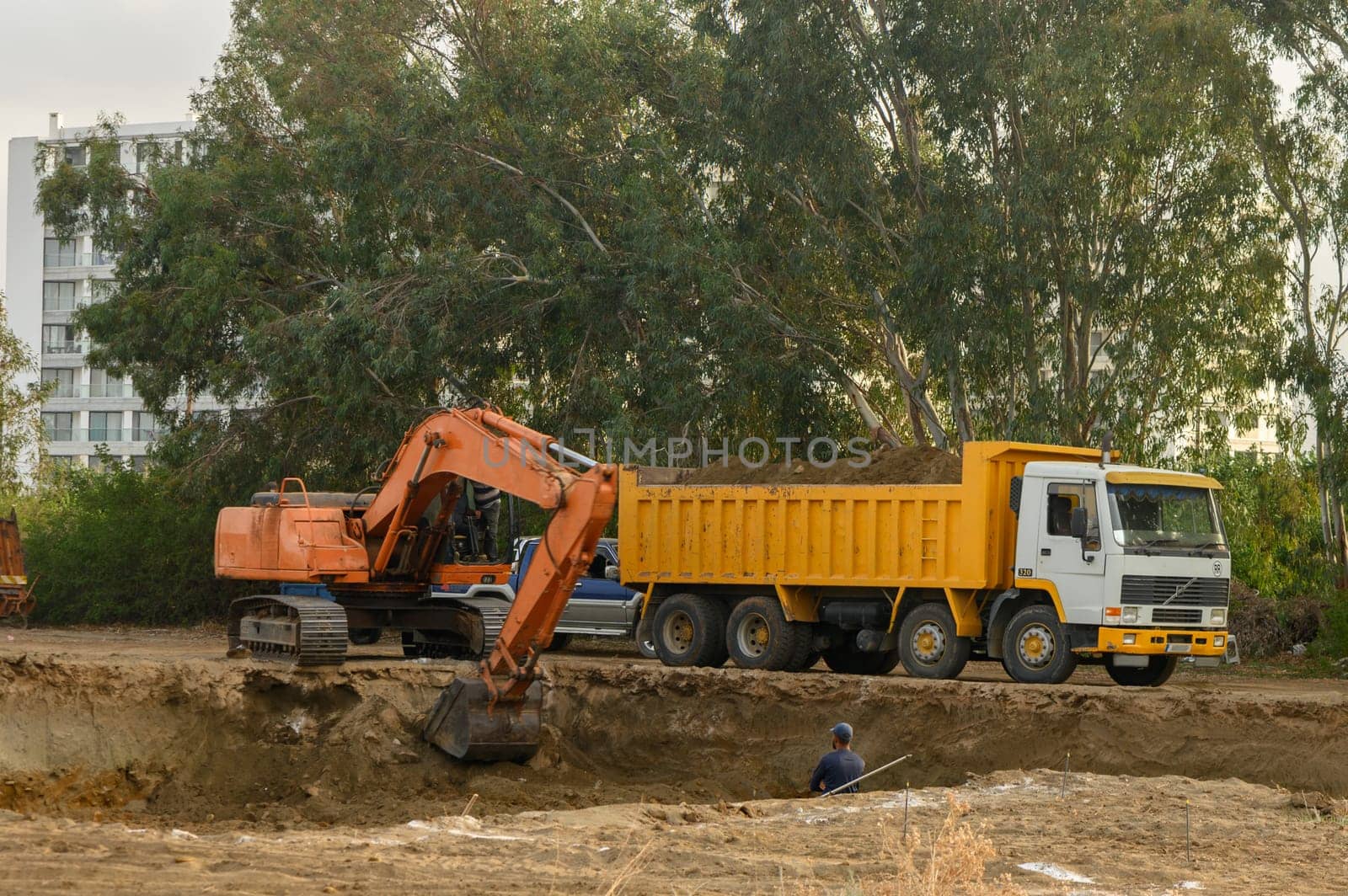 an excavator digs a hole under the foundation of a house and loads the earth into a dump truck 1 by Mixa74