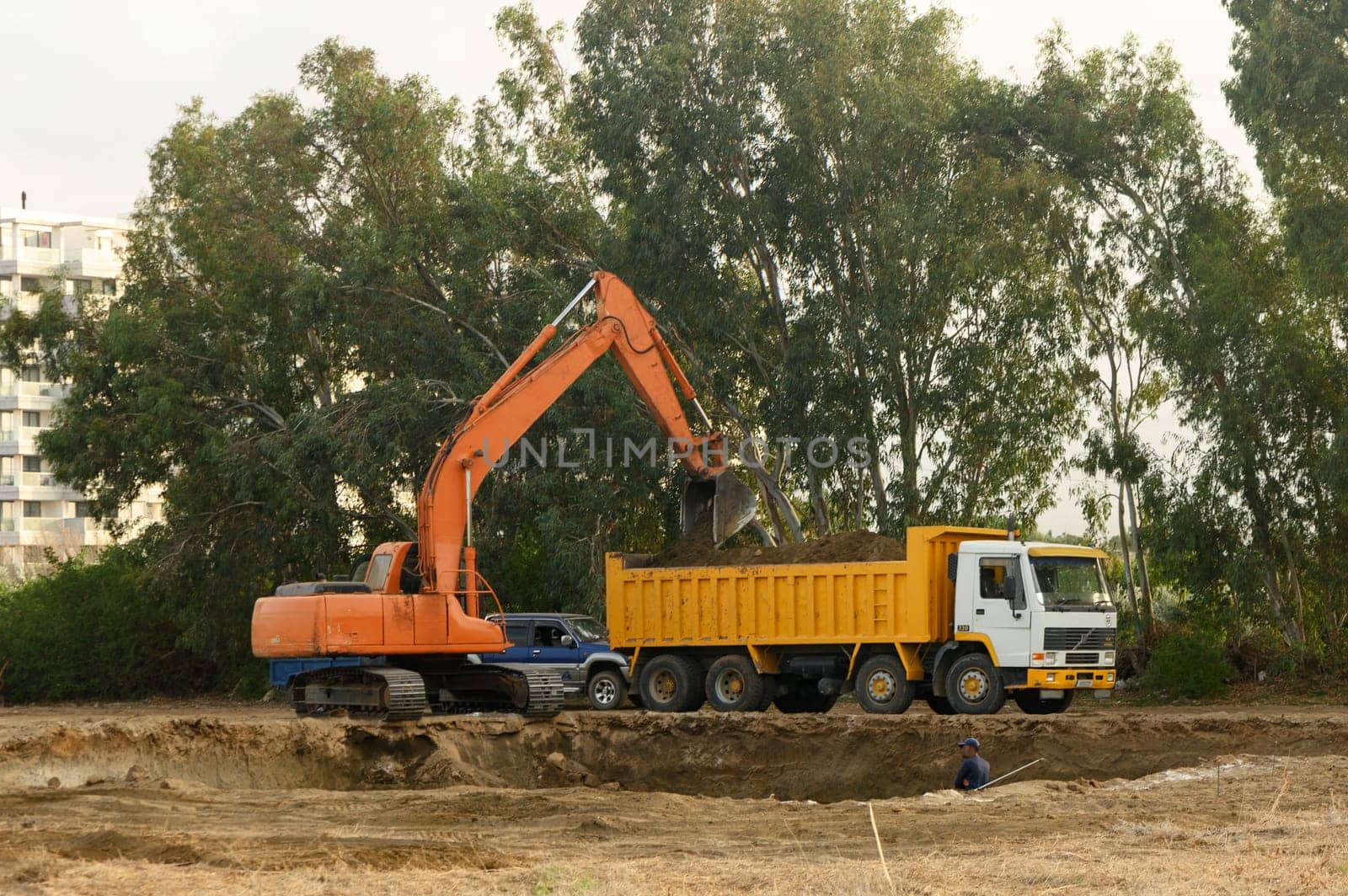 an excavator digs a hole under the foundation of a house and loads the earth into a dump truck3 by Mixa74