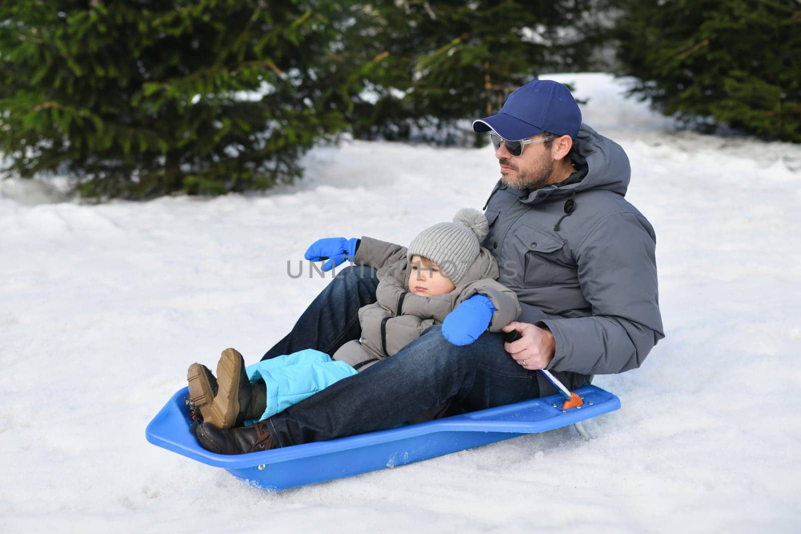 A father with child sledding in the snow by Godi