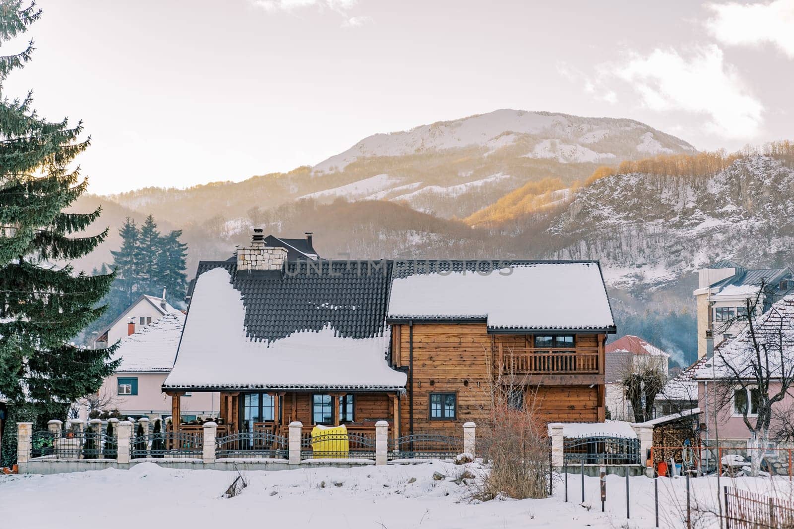 Two-story wooden cottage in a snowy village at the foot of the mountains. High quality photo