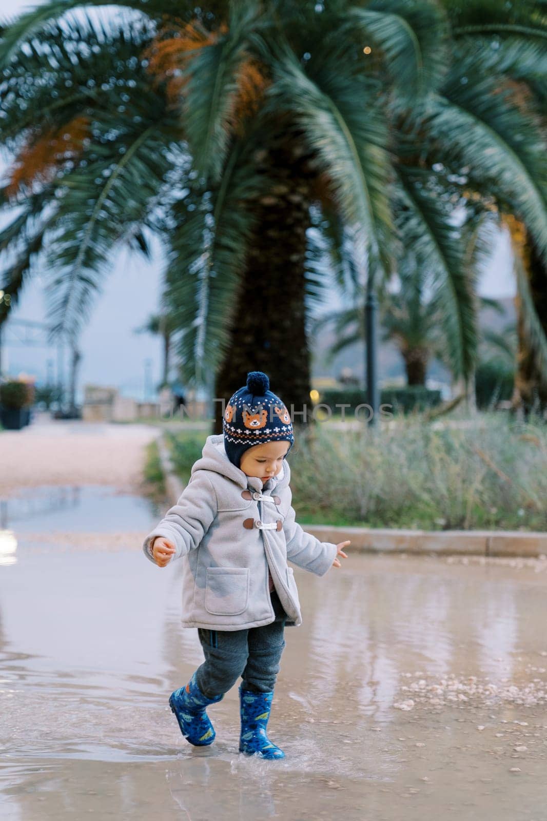 Little girl in rubber boots walks in a puddle in the park. High quality photo