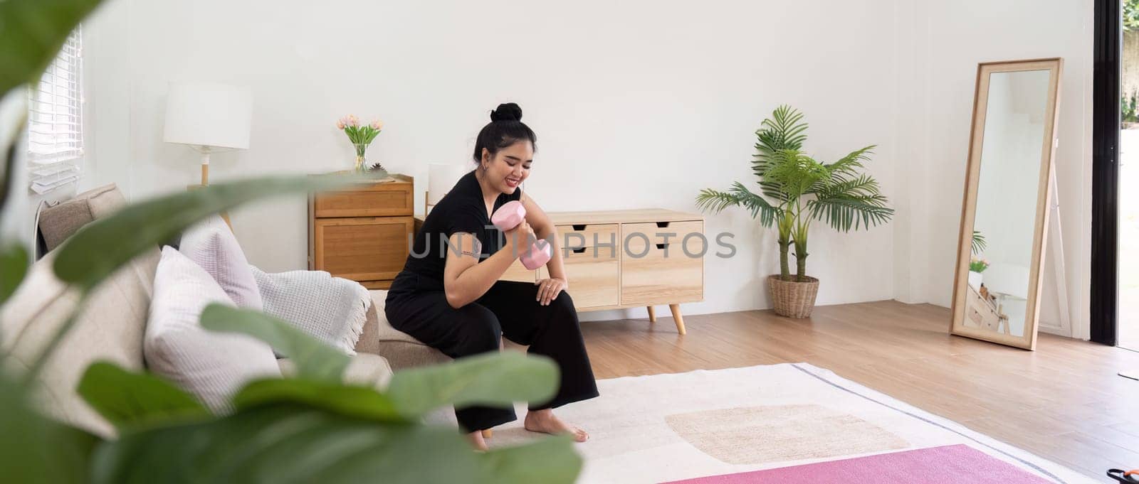 Happy overweight woman doing exercise with dumbbell fitness at home by nateemee